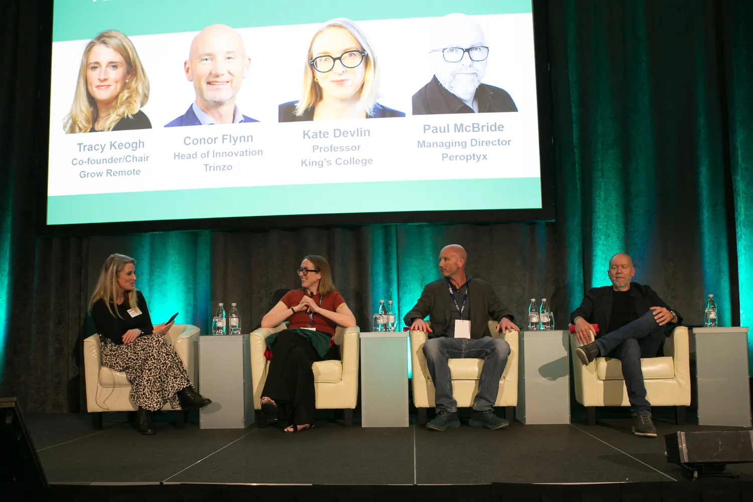 A four-person panel on stage at the Amplify Innovation Summit, speaker name cards displayed on the screen behind them.