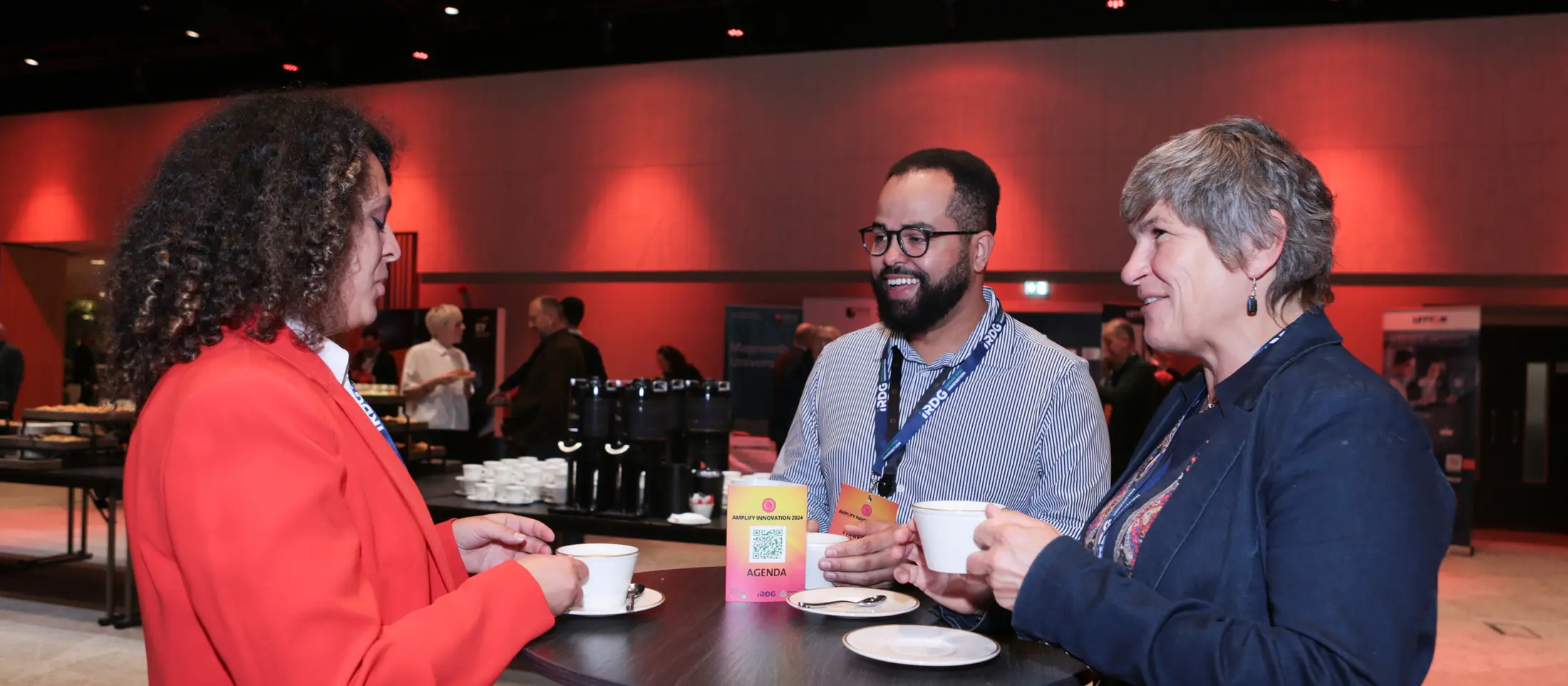 Three IRDG members in conversation over coffee at a network event.