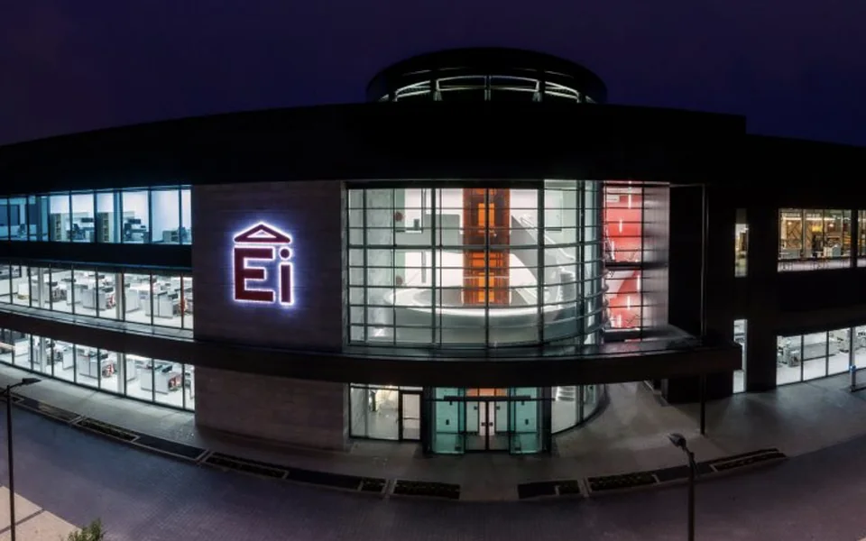 Ei Electronics' headquarters in Shannon at dusk — the curved glass frontage lit from inside, the Ei mark on the facade.